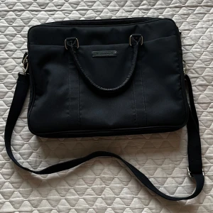 Marinblå datorväska - Snygg och praktisk marinblå datorväska med axelrem och handtag. Väskan har flera fack med dragkedja för enkel organisering av dina tillhörigheter. Perfekt för att bära din laptop och andra viktiga saker. Köptes från Zalando och har knappt kommit till användning så därav är skicket som ny.