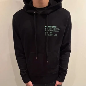 Svart hoodie från Helmut Lang - Säljer en stilren svart hoodie från Helmut Lang med tryck på framsidan. Storlek S men passar M. Bara att höra av er vid frågor! Kan eventuellt ta byten