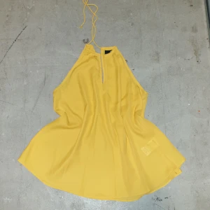 Gul halterneck topp från Gina Tricot - Snygg gul halterneck topp från Gina Tricot i ett lätt och luftigt polyester material. Toppen har en knytning i nacken och en stilren design som passar perfekt för varma dagar.