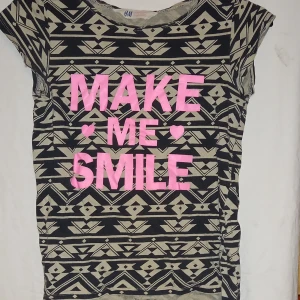 Mönstrad t-shirt från H&M med text, för barn - Cool t-shirt från H&M med ett geometriskt mönster i svart och beige. Framsidan har texten 'MAKE ME SMILE' i rosa. Perfekt för en avslappnad stil. Barn storlek 146-152 