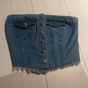 Jeanskjol med knappar - Trendig jeanskjol med knappar framtill och fransig nederkant. Kjolen har dekorativa fickor och elastisk rygg för bättre passform. Perfekt för en avslappnad stil.