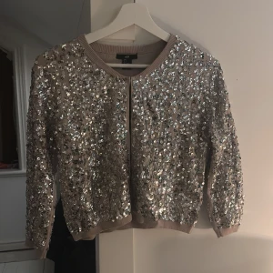Glittrig bolero/kofta - Säljer en extremt snygg glittrig bolero/kofta täckt med silverpaljetter. Koftan har korta ärmar och en rund halsringning. Perfekt för att lysa upp vilken outfit som helst! ✨