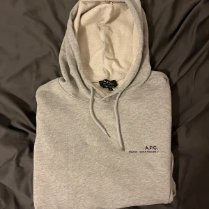 Grå hoodie från A.P.C. - Säljer en stilren grå hoodie från A.P.C. med justerbar huva och tryck framtill. Perfekt för dig som är runt 178 lång. Bra till hösten och vintern för laget på lager, men även en bra tunnare hoodie för sommarkvällar och tidig/sen vår. Jättebra skick. Hör av er vid funderingar!