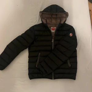 Svart pufferjacka från Colmar - Snygg svart pufferjacka från Colmar med huva och dragkedja. Perfekt för kyliga dagar med sin quiltade design och långa ärmar. Jackan har en stilren look med Colmar-logga på bröstet. Finns några defekter, skriv till mig för bilder på de. Passar i M/L