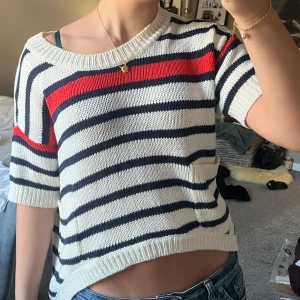 Randig stickad tröja från Vero Moda - Säljer en snygg randig tröja från Vero Moda i vitt, marinblått och rött. Tröjan är stickad och har korta ärmar med en croppad passform. Perfekt för en avslappnad stil.