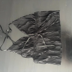 Svart ribbad linnetopp - Snygg svart ribbad linnetopp med knytband. Perfekt för en stilren look. Toppen har en vågig textur och smala axelband. PRIS KAN DISKUTERAS