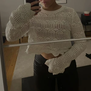 Vit virkad croppad tröja - Säljer en snygg vit virkad tröja med croppad passform. Tröjan har långa ärmar och ett vackert mönster som ger en bohemisk känsla. Perfekt för lager-på-lager-stil eller som statement-plagg.