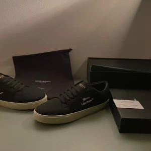 Svarta sneakers från Saint Laurent - Snygga svarta sneakers från Saint Laurent med vit sula och märkets logga på sidan. Skorna har en klassisk design med snörning och är perfekta för en stilren look.