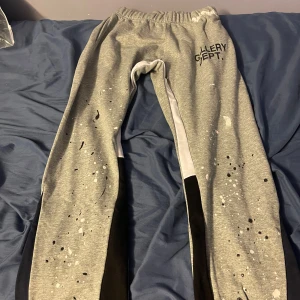 Grå mjukisbyxor från Gallery Dept. - Snygga grå mjukisbyxor från Gallery Dept. med unikt stänkmönster. Byxorna har elastisk midja och svarta detaljer längs benen. Perfekta för en avslappnad stil. Lite i storlek 
