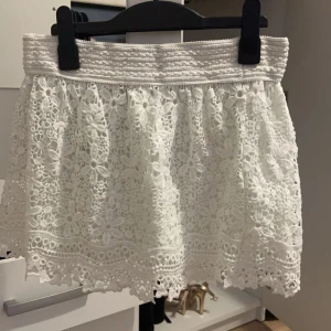 Vit spetskjol - Charmig vit kortkjol i spets med vackra blommönster. Perfekt för en somrig look med sin luftiga design och elastiska midja för bekväm passform.