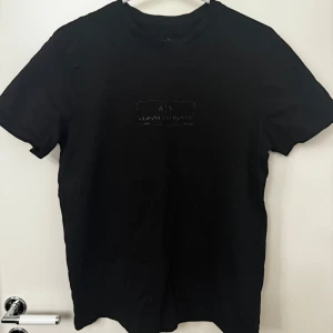 Svart t-shirt från Armani Exchange - Snygg svart t-shirt från Armani Exchange med diskret logga på bröstet. Perfekt för en stilren look. Kortärmad och i mjukt material för bekväm passform.