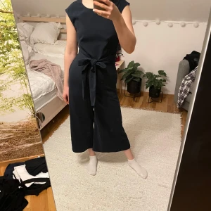 Marinblå jumpsuit från Vila - Snygg marinblå jumpsuit från Vila med knytband i midjan. Den är ärmlös och har vida ben. Mycket fint skick.