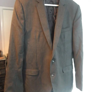 Randig kavaj från Dolce & Gabbana - Snygg randig kavaj från Dolce & Gabbana i en klassisk grå nyans. Kavajen har två knappar framtill och stilrena detaljer med märkets logga på knapparna. Perfekt för en elegant look.