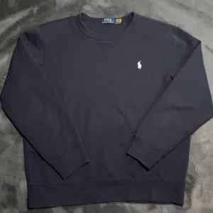 Ralph Lauren sweatshirt - Säljer en stilren mörkblå sweatshirt från Polo Ralph Lauren med det klassiska broderade logotypen på bröstet. Tröjan har långa ärmar och ribbade muddar vid ärmslut och nederkant. Perfekt för en avslappnad look. Storlek L men passar även M. Nypris 2000kr, skick 10/10. Har inget äktahetsbevis. Pris går att diskutera ✅