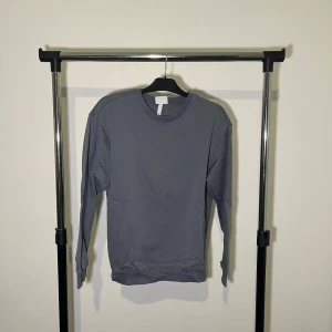 Grå tröja från H&M Essentials - Säljer en stilren grå tröja från H&M Essentials i storlek S. Tröjan har en relaxed fit och är perfekt för en avslappnad look. Den är långärmad och har ribbade muddar vid ärmslut och nederkant.