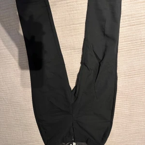 Svarta byxor med hyska och hake - Snygga svarta byxor med hyska och hake i midjan. Perfekta för en stilren look. Byxorna har en smal passform och är tillverkade i ett mjukt material för extra komfort.