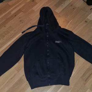 Säljer en svart hoodie från Strike Pro i mycket bra skick. Den har en dragkedja framtill och en stor logga på ryggen samt ärmen. Perfekt för höst och vinter, med en skön passform och huva för extra värme. Perfekt för casual dagar eller fiskeäventyr! 🎣