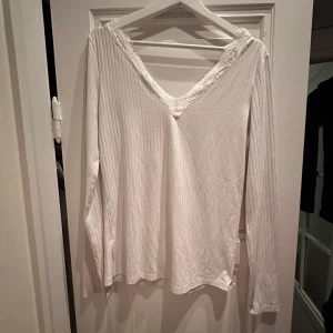 Vit ribbad långärmad topp med spetsdetaljer - Säljer en superfin vit ribbad topp med långa ärmar och v-ringning. Den har snygga spetsdetaljer runt halsen. Perfekt för både vardag och fest! 🕊️skrynklig pga legat i påse på vinden