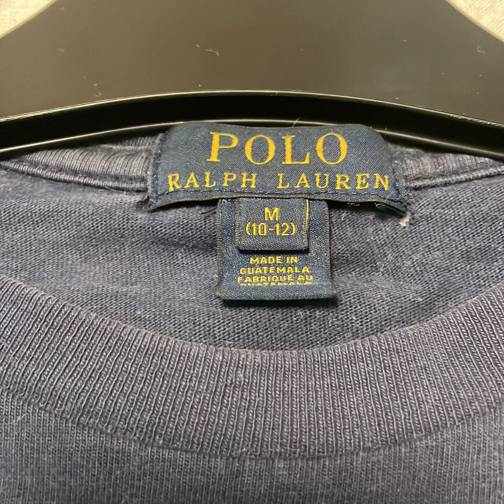 Säljer en klassisk mörkblå t-shirt från Polo Ralph Lauren i storlek M dock för åldrar 10-12. Den har en röd broderad logga på bröstet och är gjord av mjuk bomull. Perfekt för en avslappnad stil eller sommarens äventyr. Passar till allt!. T-shirts.