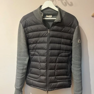 Moncler Cardigan - Tjena! Säljer min Moncler cardigan i storlek M pga att den knappt kommer till användning. Den är i bra skick men har en liten skada längst fram på ärmen men inget som påverkar utseendet! Hör av dig om du har några frågor eller vill ha flera bilder!🤩