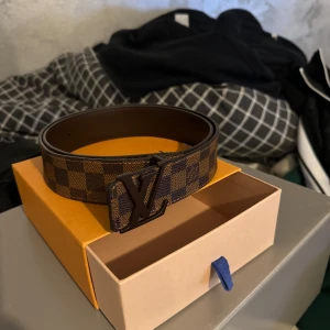 Lv bälte - Säljer ett snyggt brunt rutigt bälte från Louis Vuitton. Bältet har en stor LV-logga som spänne och är i mycket bra skick. Perfekt för att ge din outfit en lyxig touch. Kommer i originalförpackning. Passar både till vardag och fest! 90cm!