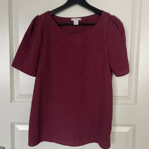 Mönstrad vinröd blus - Säljer en superfin vinröd blus med små vita mönster. Den har korta ärmar och en rund halsringning. Perfekt för både vardag och fest! 🥳