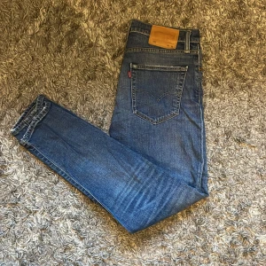 Blå jeans från Levi's - Säljer ett par klassiska blå Levi's jeans i bra skick. De har en liten slitagefläck på benet men är annars i fint skick. Perfekta för vardagsbruk med en snygg straight passform och midwaist. Passar både till avslappnade och mer uppklädda tillfällen.