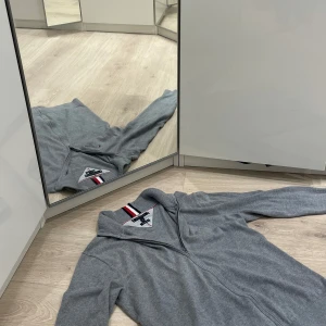 Tommy Hilfiger kofta  FULLZIP - Säljer en stilren grå tröja från Tommy Hilfiger i premium bomull. Tröjan har en dragkedja framtill och en ribbad krage med klassiska ränder i rött, vitt och blått. Perfekt för både vardag och lite finare tillfällen. Passar bra till höst och vår!