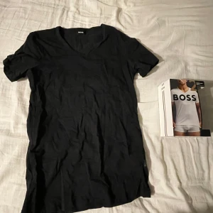 2 Svarta t-shirts från Boss - Säljer en stilren svart t-shirt från Boss i mycket bra skick. Den är kortärmad och har en v-ringad design, perfekt för både vardag och fest. Materialet känns mjukt och skönt mot huden. Tröjorna är helt nya bara provade.