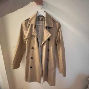 Säljer en snygg beige trenchcoat i bra skick. Den har klassiska svarta knappar och ett bälte i midjan för en stilren look. Perfekt för höst och vår! 🧥