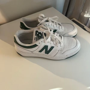 Vita och gröna sneakers från New Balance 480 - Säljer ett par snygga vita sneakers från New Balance med gröna detaljer. Skorna har snörning och är i mycket bra skick. Perfekta för både vardag och träning! Som nya bara använda en gång.