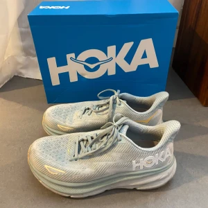 Hoka W Clifton 9 storlek 40 2/3 - Hoka W Clifton 9 i färgen cloud blue/ice. Storlek 40 2/3. Sparsamt använda inomhus och lite utomhus, säljs pga för liten storlek. Nypris 1999 kr. 