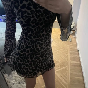Leopardmönstrad klänning med öppen rygg - Säljer en superfin leopardmönstrad klänning med öppen rygg. Den har långa ärmar och en kort passform som är perfekt för fest. Klänningen är i mycket bra skick och ger en snygg och trendig look.