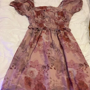 Blommig klänning med puffärmar - Säljer en superfin blommig klänning med puffärmar och smockdetaljer i midjan. Den har en romantisk stil med rosa och lila toner, perfekt för vår. Klänningen är i mycket bra skick och har en luftig passform. Perfekt  för en festlig tillställning! 🌸mjuk material säljs för 70