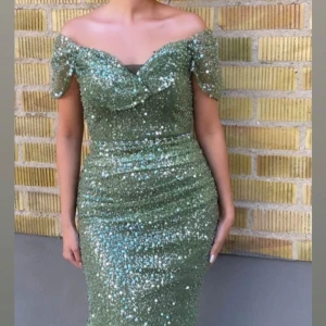  Fest klänning - Säljer en fantastisk grön glittrig klänning med offshoulder-design. Klänningen är figurnära och har en elegant slits framtill. Perfekt för festliga tillfällen där du vill glänsa! ✨