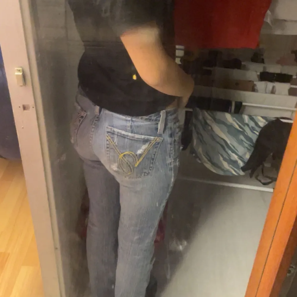 Säljer ett par snygga blå bootcut jeans från Bebe i storlek 26. De har en klassisk femficksdesign och är dekorerade med guldfärgade broderier på bakfickorna. Perfekta för en avslappnad vardagslook eller en utekväll. Skicket är bra och de är tillverkade i USA.. Farkut & Housut.