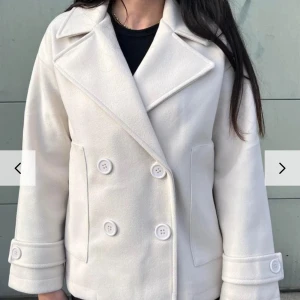 vit designbysi kappa  - Säljer en stilren vit kappa från designbysi, i mycket bra skick. Den har en klassisk design med stora knappar framtill och långa ärmar. Perfekt för höst, vår och vinter, och funkar lika bra till vardags som till fest. Storleken är normal och materialet känns mjukt och bekvämt.