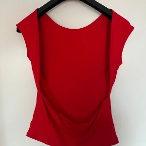 Röd ärmlös topp med öppen rygg - Snygg röd topp från Gina i ett stilrent och modernt snitt. Den är ärmlös och har en djärv öppen rygg som ger en elegant touch. Perfekt för sommarens fester eller en utekväll. Materialet känns mjukt och bekvämt mot huden.