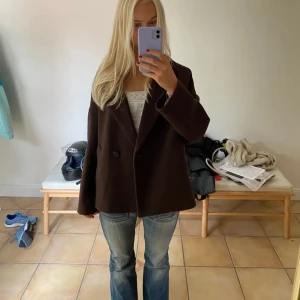 Brun kavaj - Säljer en snygg brun kappa i mycket bra skick. Den har en klassisk design med knappar framtill och långa ärmar. Perfekt för höst och vår, och funkar både till vardags och fest. Passar bra med jeans för en avslappnad look.