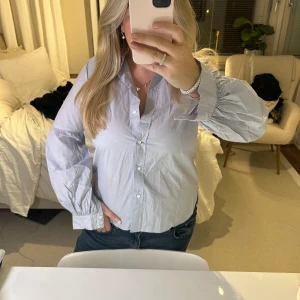Ljusblå blus med ballongärm - Säljer en ljusblå blus med knappar framtill. Den har långa ärmar med en liten puff och är perfekt för både vardag och fest. Blusen är i bra skick och passar till jeans eller kjol. Perfekt för vår och sommar!