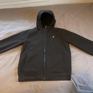 Svart jacka med huva från Lyle & Scott - Säljer en svart jacka med huva från Lyle & Scott i storlek 14/15 år och passar en XS/S. Jackan har en dragkedja framtill och är i mycket bra skick. Perfekt för höst och vår, med en stilren design och bekväm passform. Nypris 1100kr
