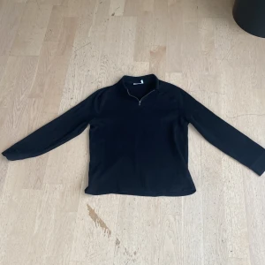 Svart tröja med dragkedja från Weekday - Säljer en stilren svart tröja från Weekday i storlek M. Tröjan har en praktisk dragkedja vid halsen och långa ärmar. Perfekt för både vardag och lite kyligare dagar. Passar till det mesta i garderoben!