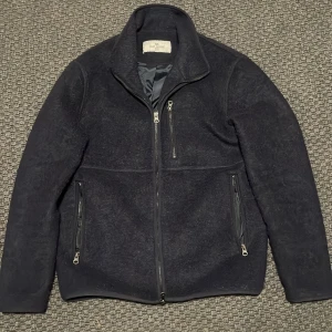 Mörkblå fleecejacka från John Henric - Säljer en snygg mörkblå fleecejacka från John Henric. Den har en dragkedja framtill och tre praktiska fickor med dragkedjor. Perfekt för kyliga dagar och ger en stilren look. Passar både till vardags och lite finare tillfällen.