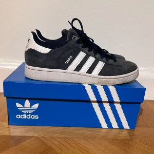 Adidas Campus sneakers - Säljer ett par Adidas Campus sneakers i mycket bra skick. De är mörkblå med vita detaljer och klassiska tre ränder på sidan. Skorna har snörning och är perfekta för vardagsbruk. De kommer i originalkartong. Nypris ligger på 1249 kr.