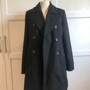 Svart kappa - Säljer en stilren svart kappa i mycket bra skick. Den har en klassisk dubbelknäppt design med långa ärmar och en elegant krage. Perfekt för höst och vinter, och funkar lika bra till vardags som till fest. Använd endast ett par gånger.