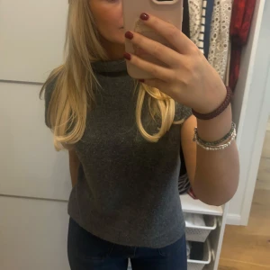 Grå ärmlös topp - Säljer en stilren grå ärmlös topp i mjukt material. Perfekt för både vardag och festliga tillfällen. Toppen har en hög krage som ger en elegant touch. Passar bra till jeans eller kjol för en avslappnad men chic look.