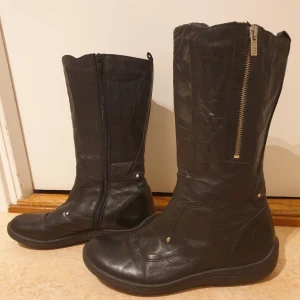 Svarta skinnstövlar med dragkedja - Säljer ett par svarta stövlar i skinn med dragkedja på sidan. De är i bra skick och perfekta för höst och vinter. Stövlarna har en klassisk design med rund tå och är bekväma att bära. Perfekta för både vardag och lite finare tillfällen. Är lättfodrade. Lite nötta på tårna, se bild.