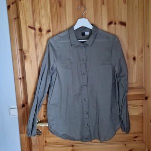 Olivgrön skjorta - Säljer en olivgrön skjorta med långa ärmar och knappar hela vägen ner. Perfekt för en avslappnad men stilren look. Skjortan är i ett mjukt och tunnt material.