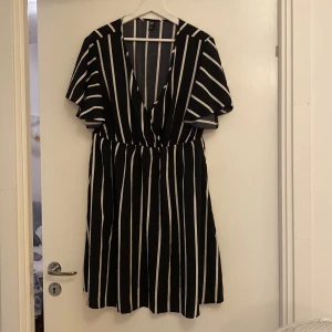 Svart och vit randig klänning - Säljer en superfin svart och vit randig klänning med korta ärmar. Den har en v-ringad design och ett elastiskt band i midjan för en bekväm passform. Perfekt för både vardag och fest!
