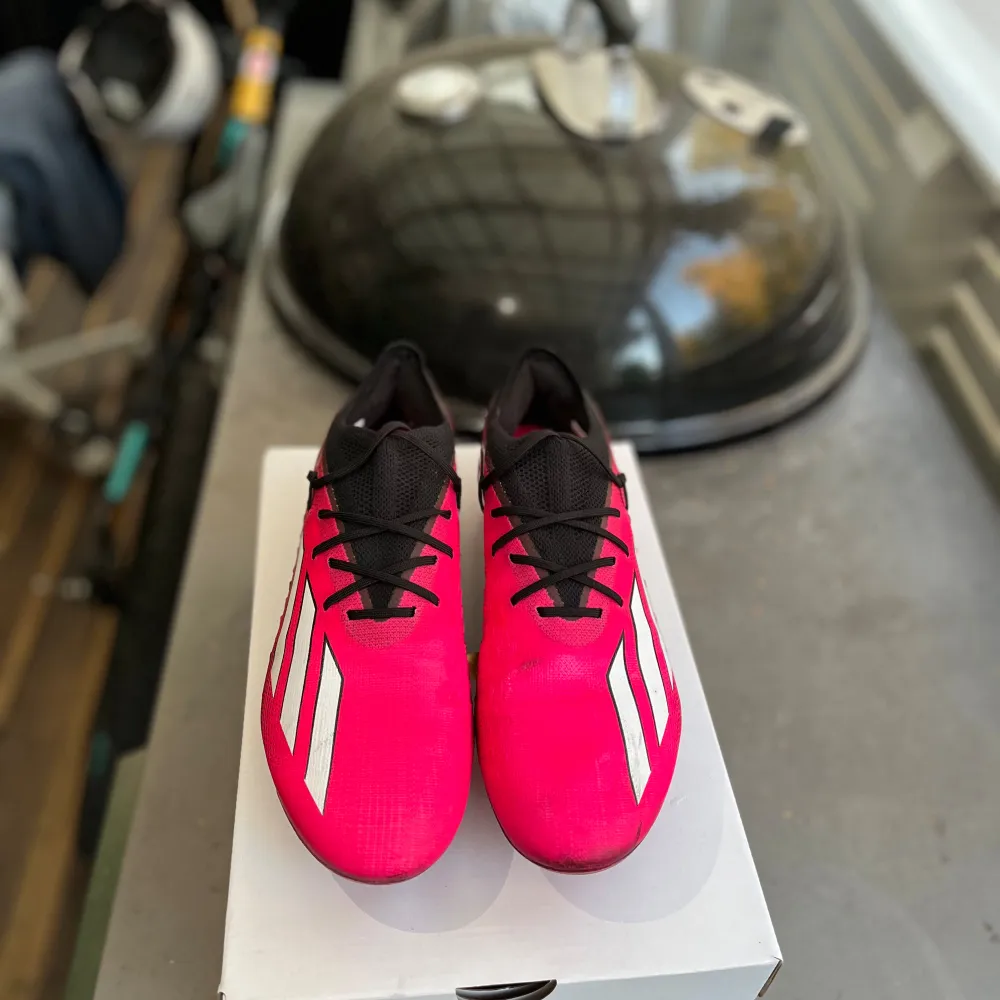 Säljer ett par snygga fotbollsskor från Adidas i rosa och svart. Skorna har en modern design med tre vita ränder på sidan och svarta snören. De är perfekta för fotbollsträning och matcher. Sulan har flera dobbar för bra grepp på planen.. Skor.